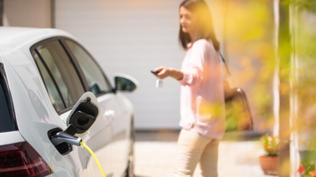 Close up of a electric car charger with female silhouette in the background, locking a car